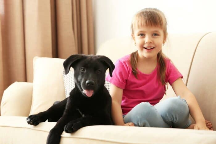 Dog Names That Start With M - Little girl sitting on couch with black Lab